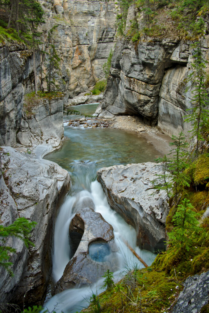 Gentle waterfall cascading over rocks surrounded by lush moss and green grass in canyon Wallpaper