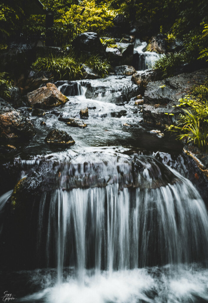 Serene waterfall cascading over smooth stones surrounded by lush greenery and soft light Wallpaper