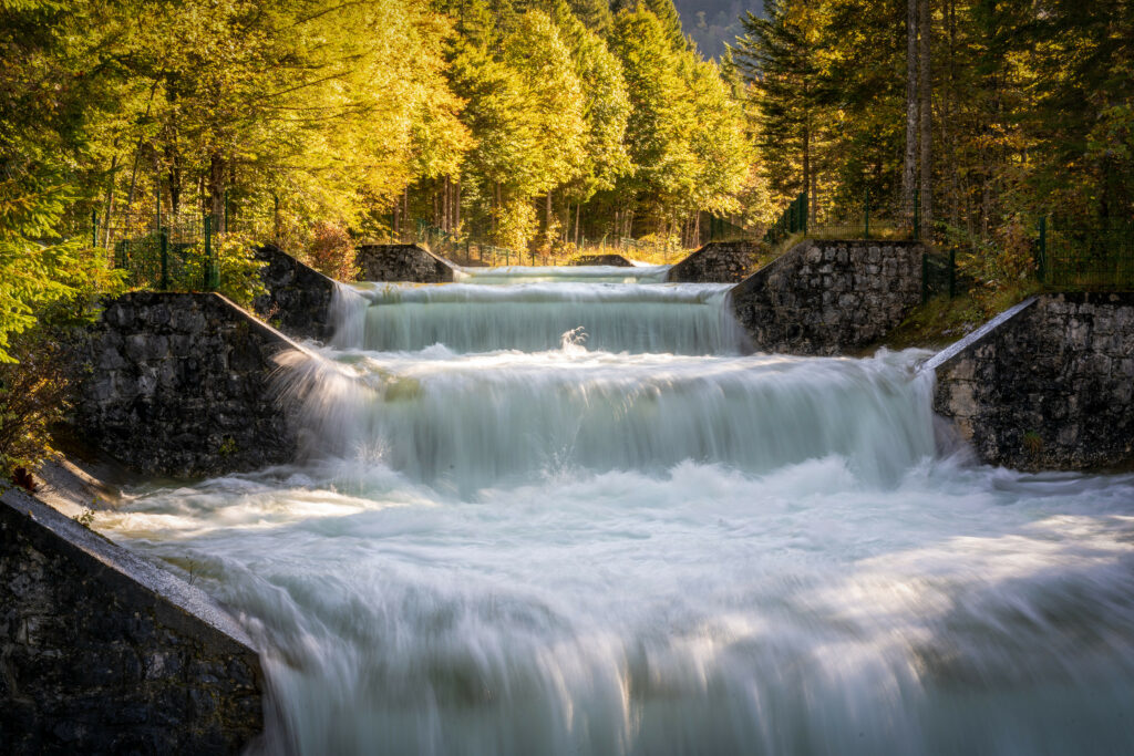 Serene waterfall over stone steps with lush green trees in warm golden sunlight wallpaper background