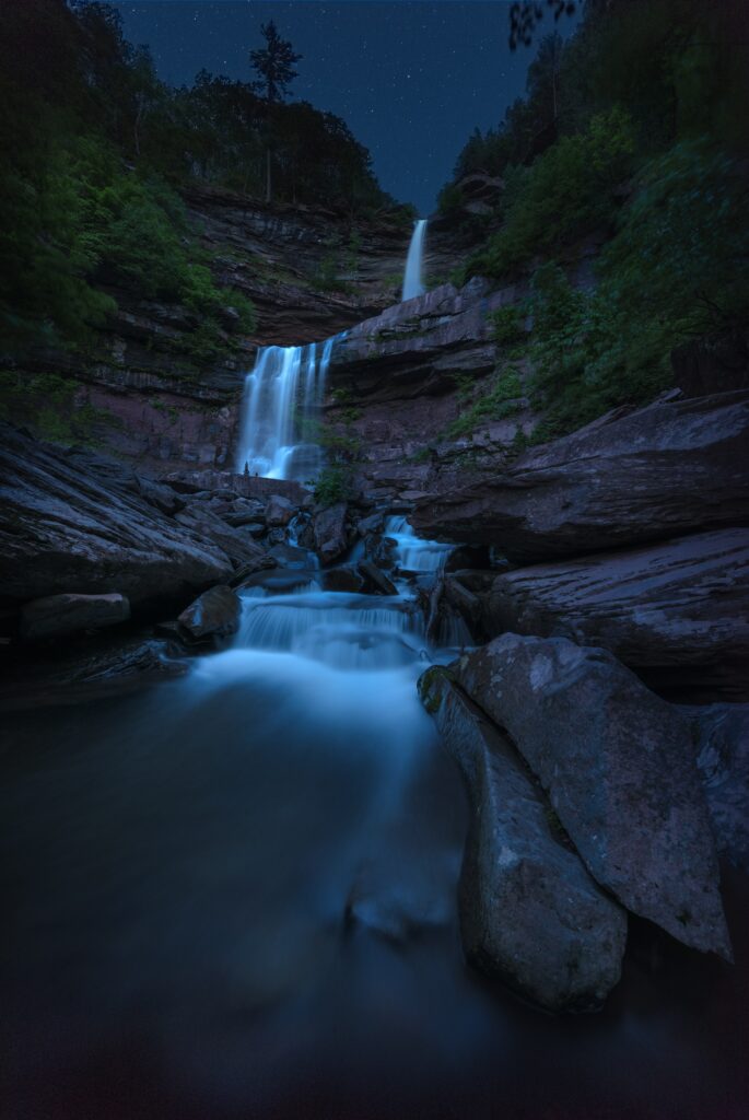 Serene waterfall cascading over rocks under starry twilight sky with lush greenery background Wallpaper