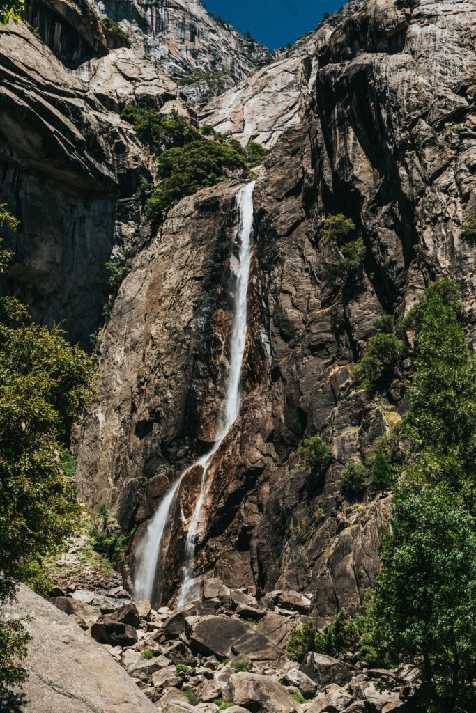 Waterfall cascading over rugged stone cliffs surrounded by rocks lush greenery natural textures Wallpaper