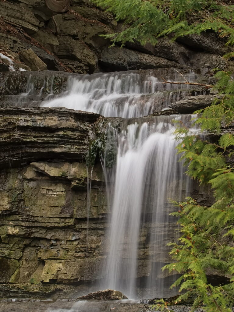 Serene natural waterfall cascading over layered rocks with lush green foliage woodland wallpaper