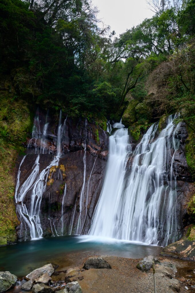 Waterfall cascading over rocky cliff with lush green trees and clear pool in natural landscape Wallpaper