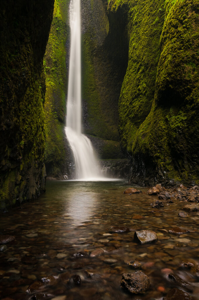 Tranquil waterfall flowing into clear pool with mossy stones and towering rock walls wallpaper
