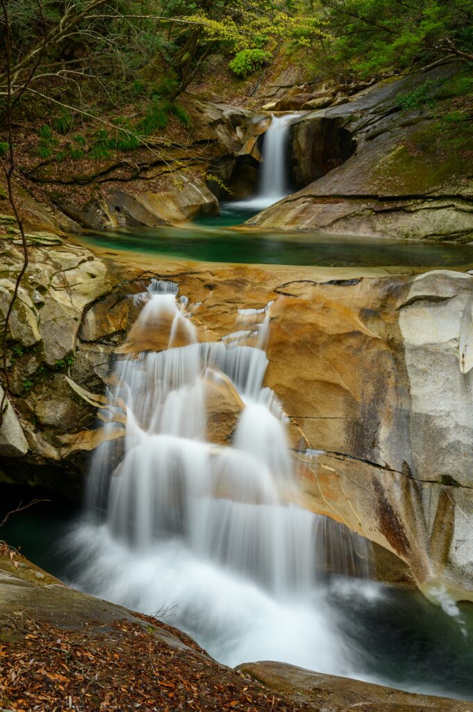 Serene waterfall cascading over smooth rocks into clear stream surrounded by lush green trees Wallpaper
