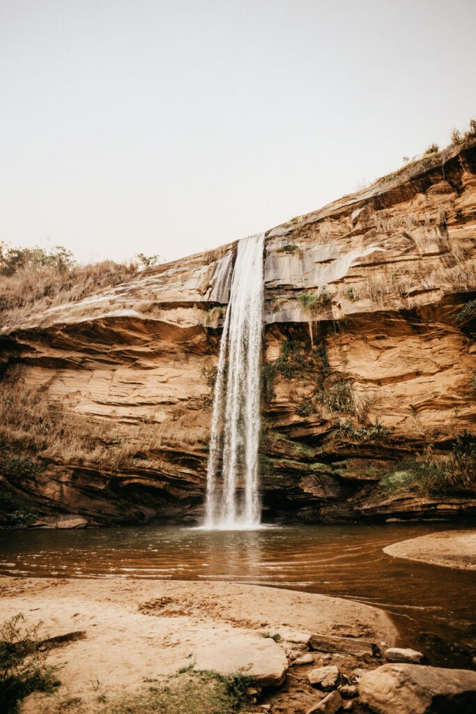 Majestic waterfall cascading down cliff surrounded by stones calm river and sandy shore wallpaper