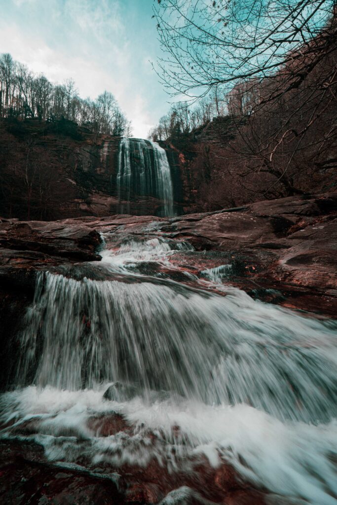 Dramatic waterfall over rugged rocks into river surrounded by bare trees in serene landscape Wallpaper