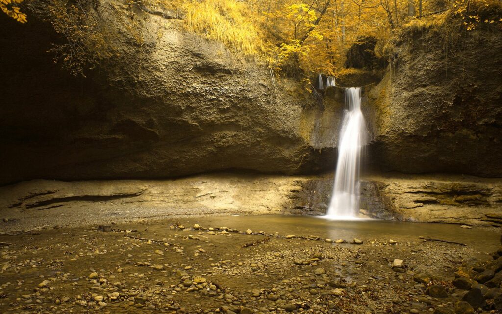 Serene waterfall over rugged rocks into tranquil pool in golden autumn garden landscape wallpaper