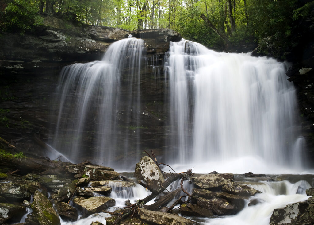 Serene waterfall cascading over stones and logs in lush green forest with misty spray wallpaper