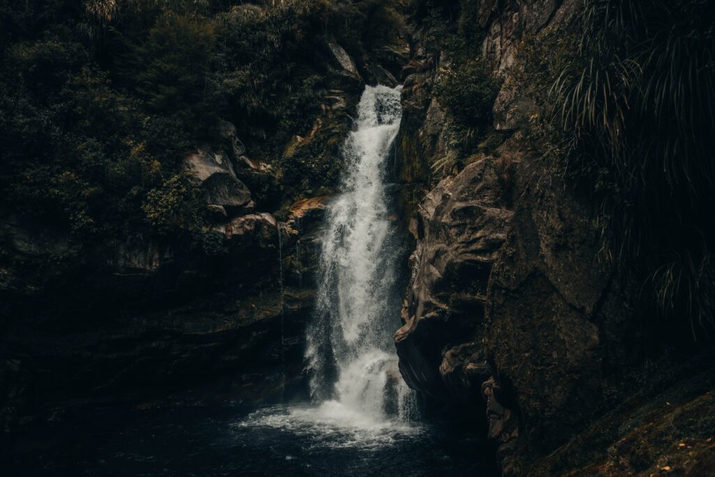 Serene waterfall cascading over rocks into dark pool surrounded by lush green forest wallpaper background