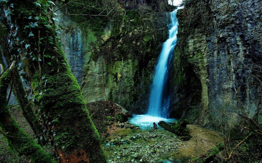Serene waterfall flowing over rugged rocks into clear pool surrounded by mossy gorge greenery Wallpaper