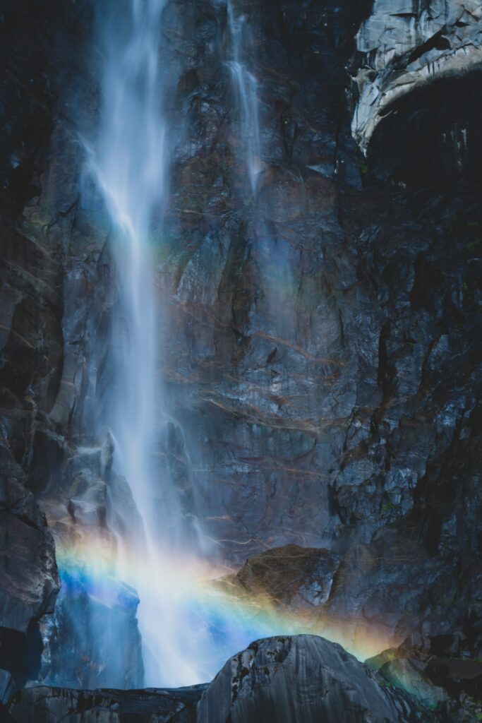 Graceful waterfall cascading over rugged blue rocks with vibrant rainbow in serene nature scene Wallpaper