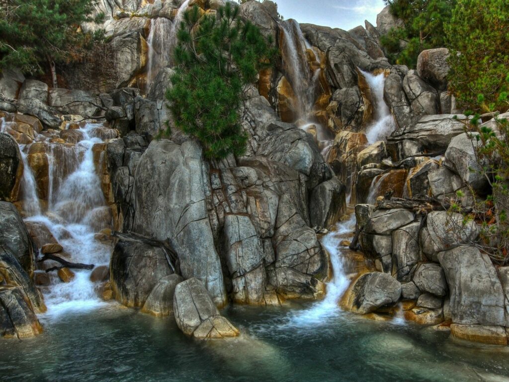 Serene waterfall cascading over rocky stones with lush greenery and vibrant blue water background Wallpaper