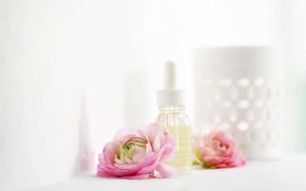 Glass dropper bottle with pink ranunculus flowers and candle warmer on white spa background Wallpaper