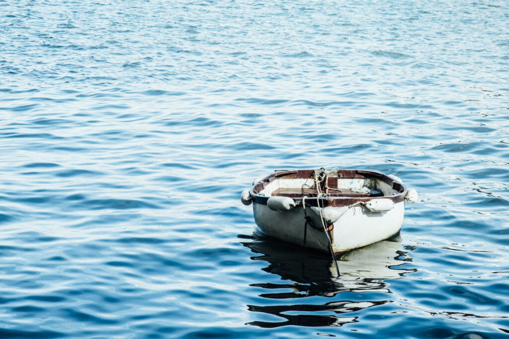 Small white boat floating on clear blue water with gentle rippling waves serene wallpaper background