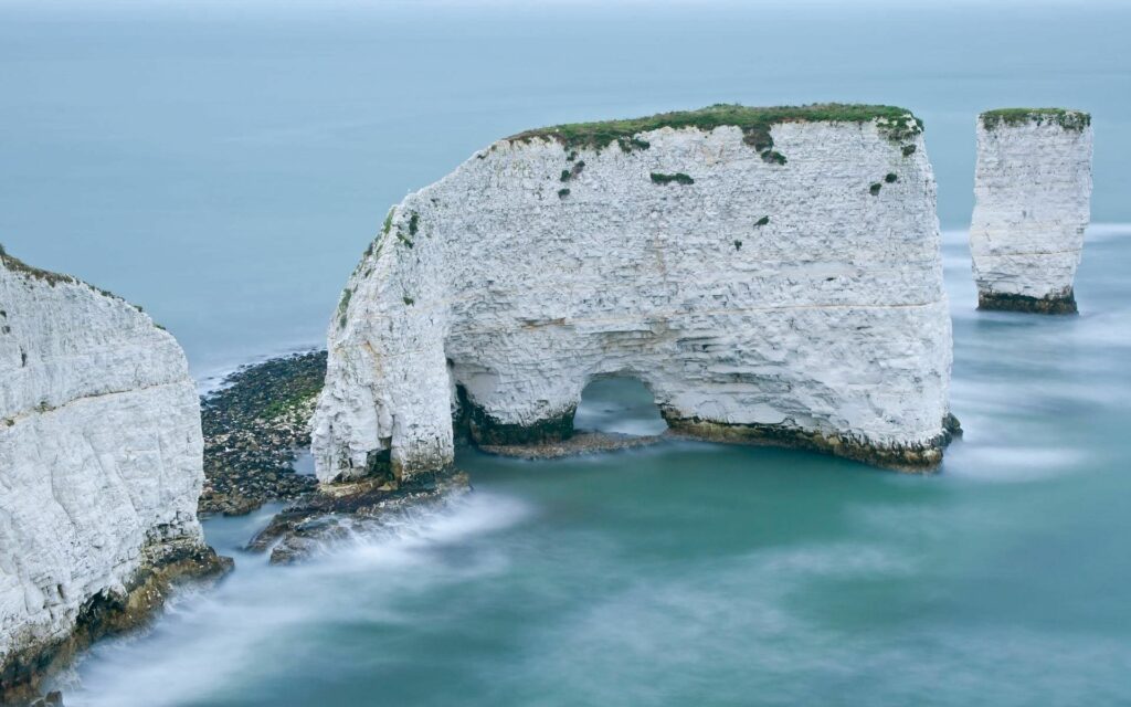 White chalk cliffs and natural rock arch at Old Harry Rocks with calm blue-green sea and mist Wallpaper