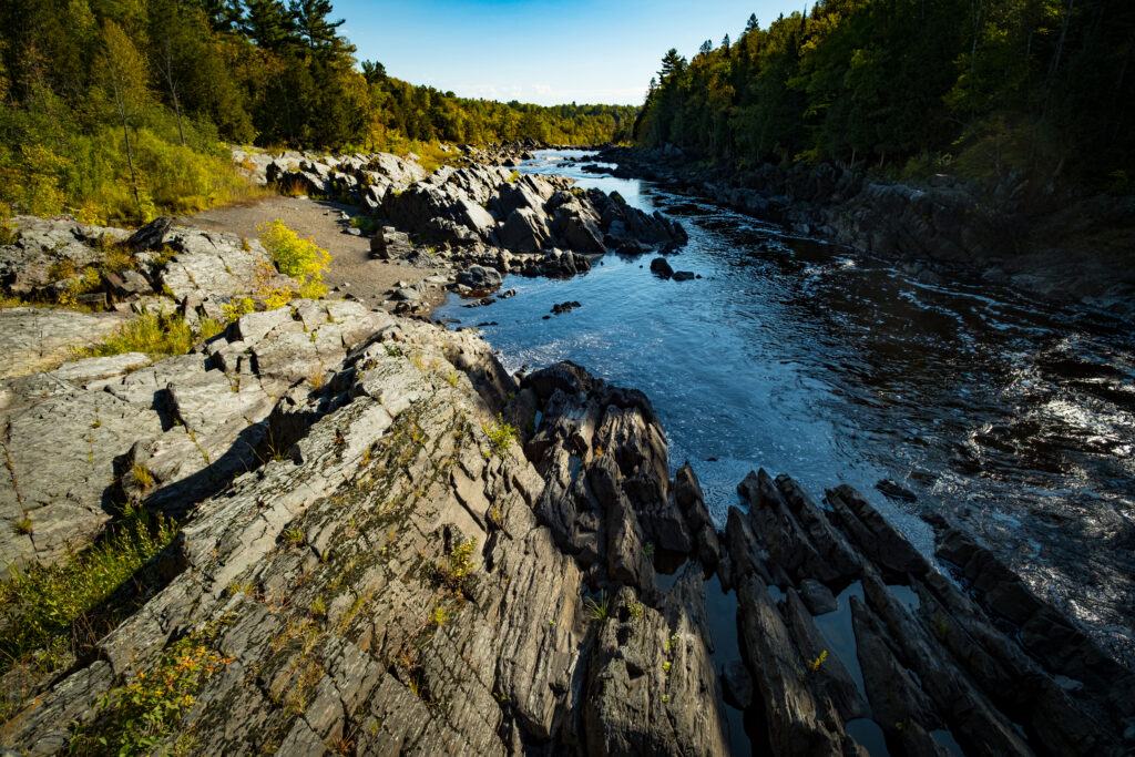 Rugged stone formations and flowing river surrounded by dense forest and vibrant greenery wallpaper