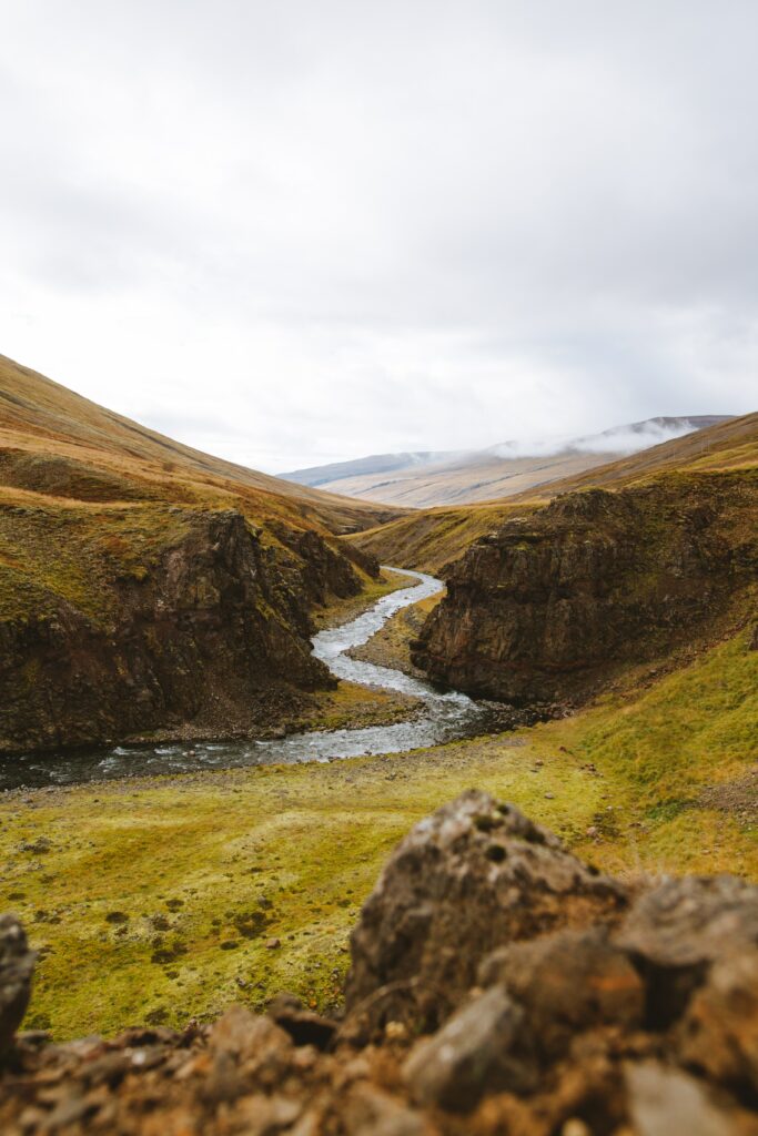 Serene winding stream through rugged hills with mossy stones under a cloudy sky wallpaper