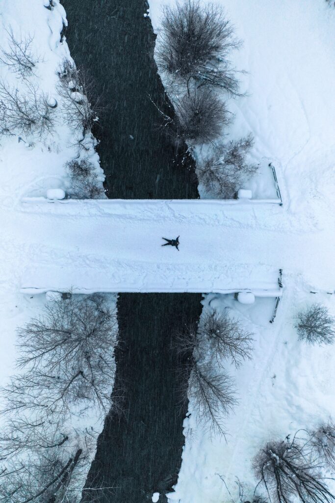 Aerial view of snowy landscape with river and man on snow-covered bridge winter wallpaper