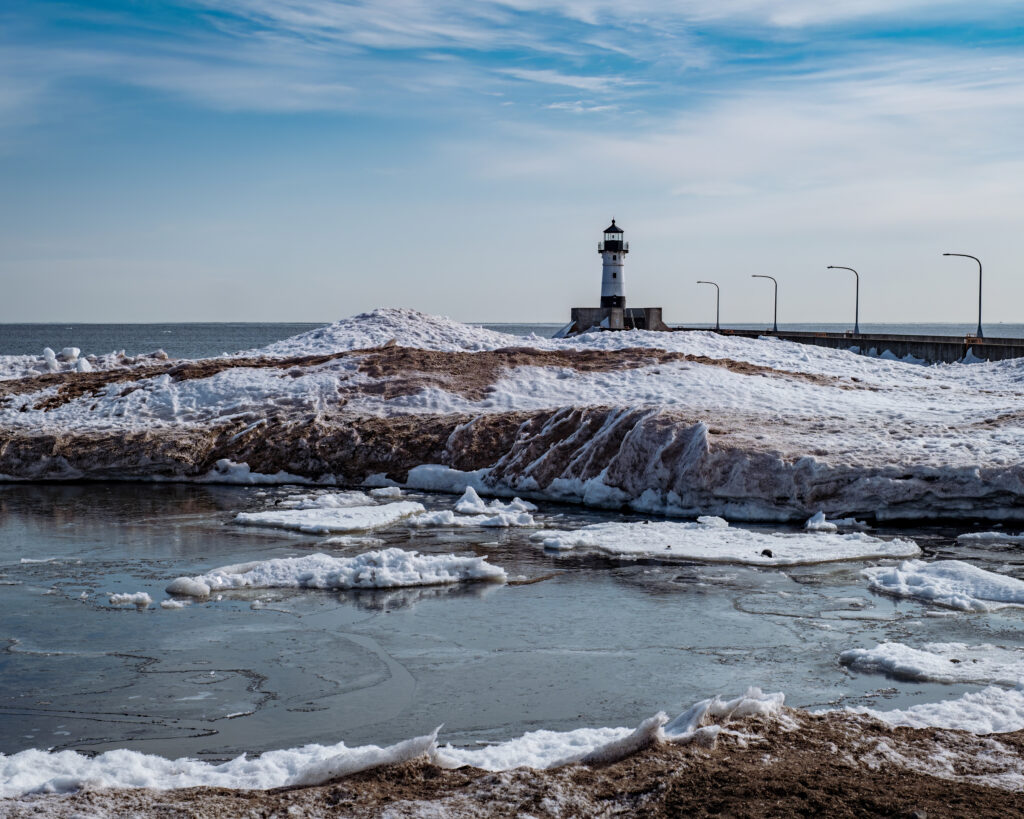 Coastal lighthouse by frozen river with snow and ice under clear blue winter sky wallpaper background
