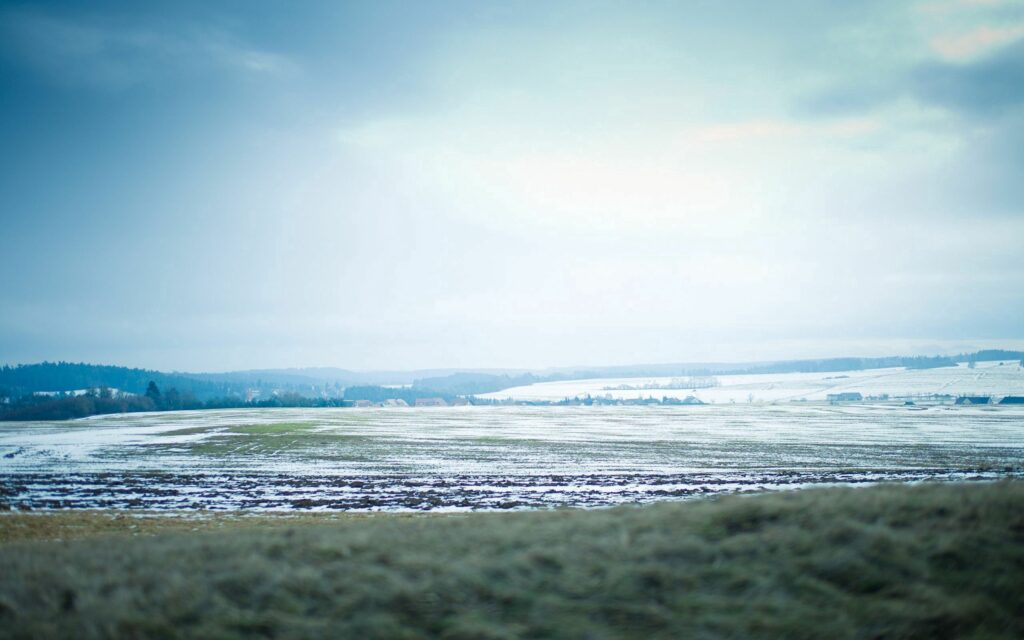 Serene winter golf course with light snow and misty fairways under pale blue sky wallpaper