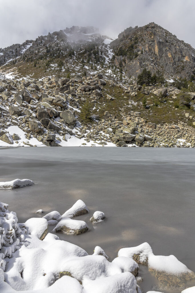 Serene winter lake with snow-covered rocks and rugged mountains in a peaceful landscape Wallpaper