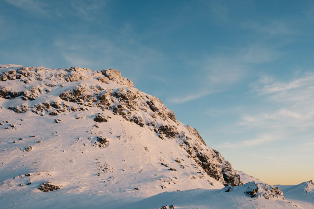 Snow-covered hill with golden sunlight rugged rocks and clear blue sky winter landscape wallpaper