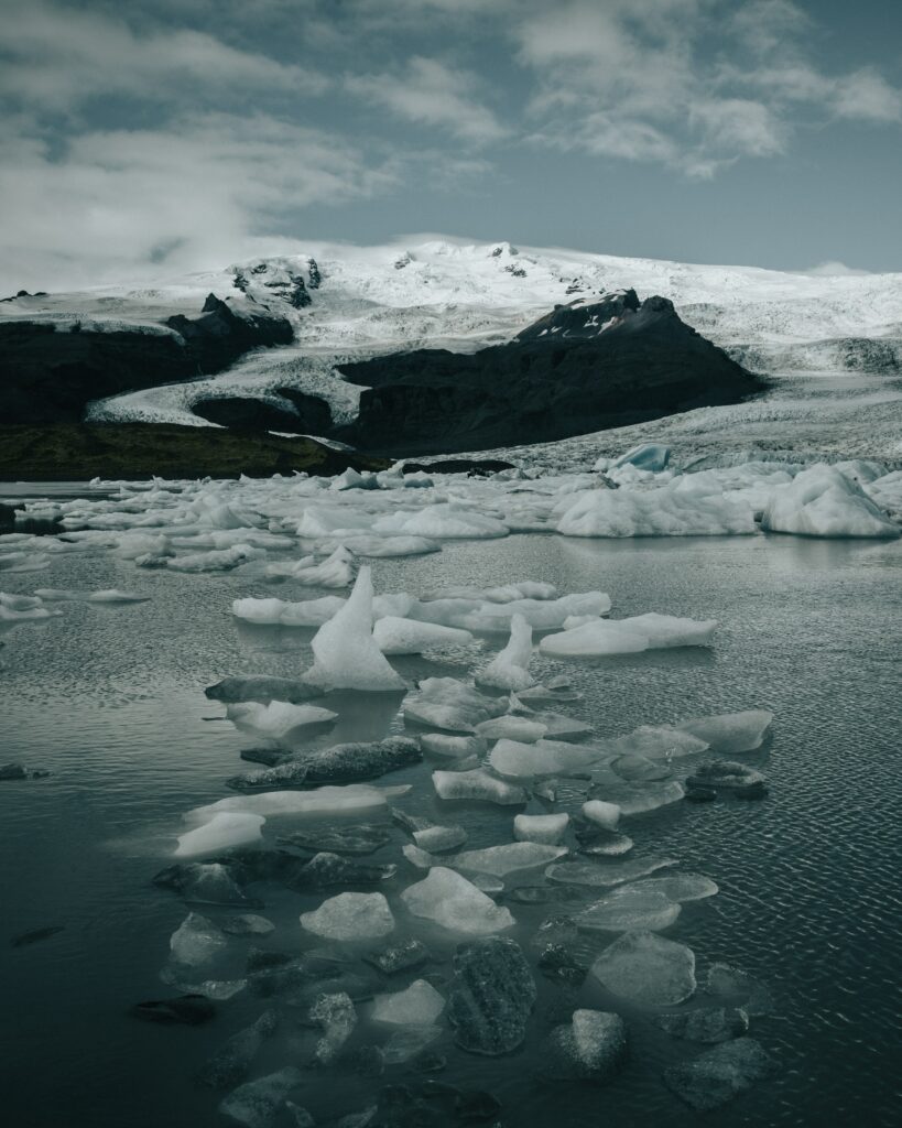 Serene winter landscape with floating ice snow-covered rocks and distant mountains under sky Wallpaper