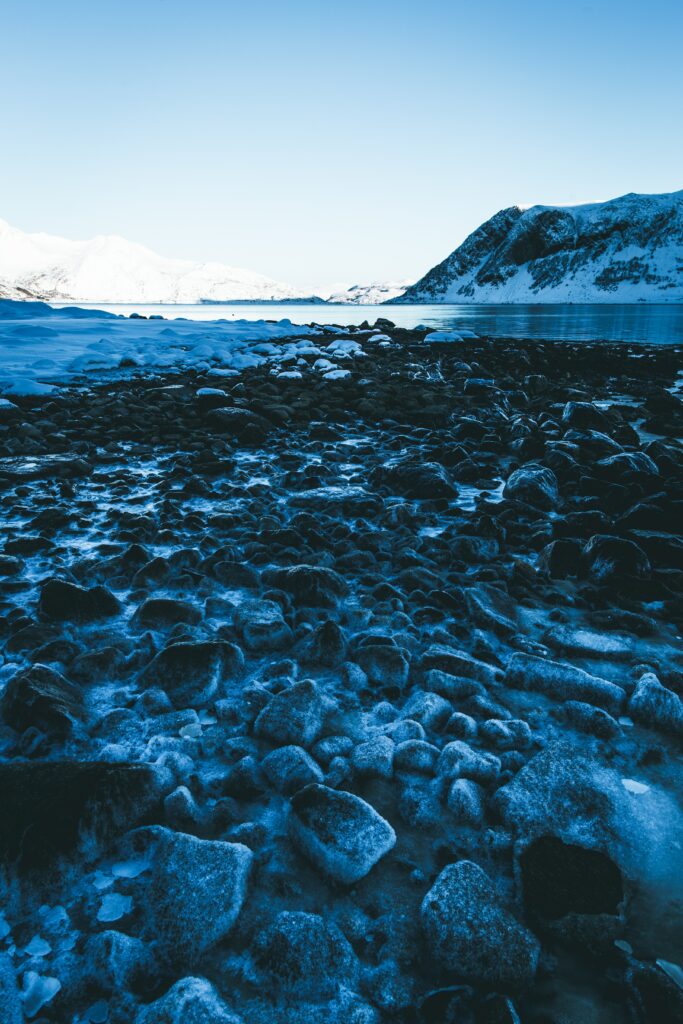 Serene winter landscape with frosty stones lake reflection snowy mountains and clear blue sky Wallpaper