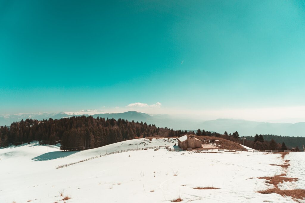 Serene winter landscape with snow-covered mountains trees rustic cabin and vibrant blue sky Wallpaper