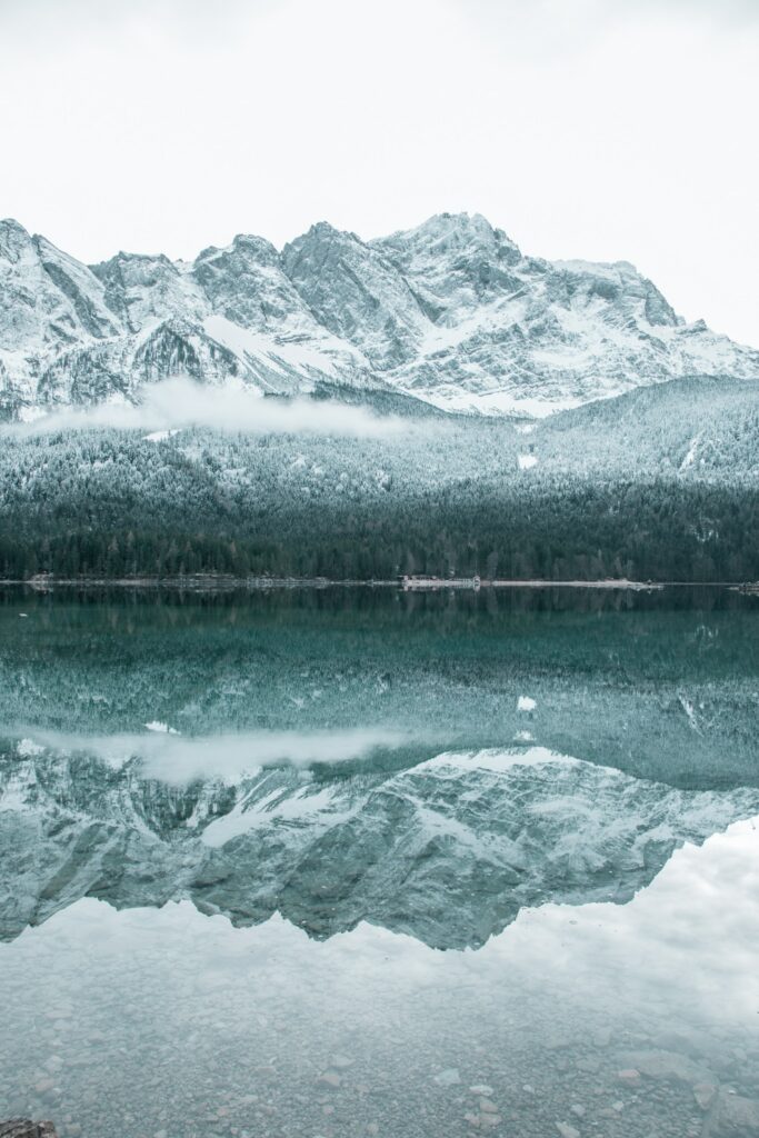 Serene winter landscape with snow-covered mountains reflected in calm blue lake wallpaper background