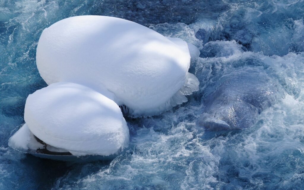 Serene winter landscape with snow-covered rocks and clear icy blue water background wallpaper