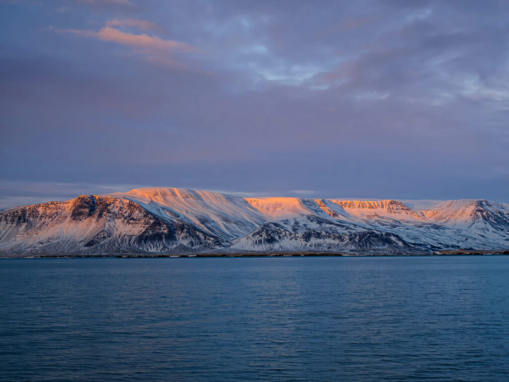 Serene winter landscape with calm sea snow-capped mountains and pastel sunset sky wallpaper background