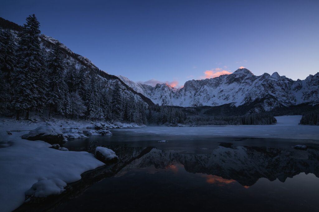 Winter mountain landscape with snow pine trees reflected in calm lake at dusk pink clouds Wallpaper