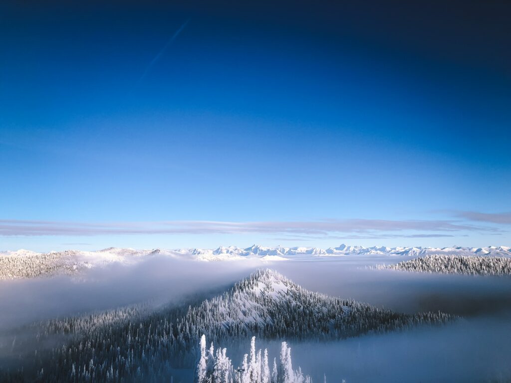 Snowy mountain peaks and pine trees under clear blue sky winter landscape wallpaper background