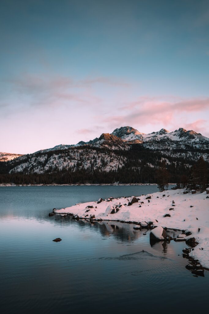 Serene winter landscape with snow-covered mountains reflected in calm lake and pink blue sky Wallpaper