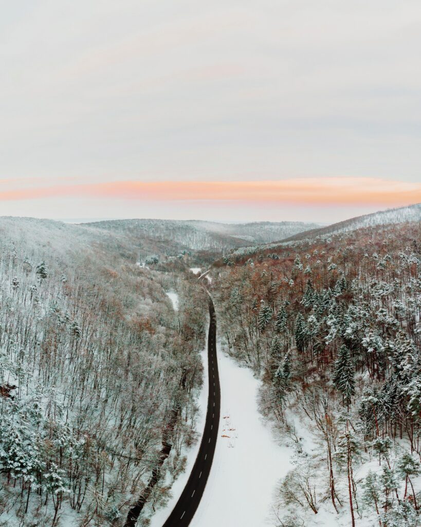 Aerial view of winding road through snow-covered mountains and forests under pastel sky Wallpaper
