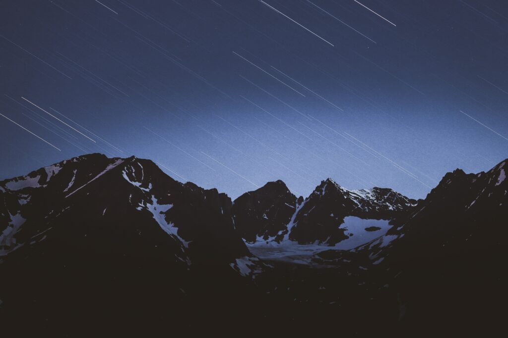 Serene night sky with starfall over snow-capped rugged mountains winter landscape wallpaper