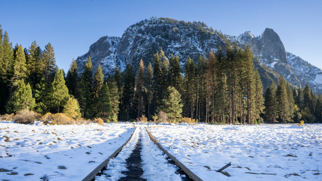 Winter railroad track through snowy forest glade with green trees and snow-covered mountains Wallpaper
