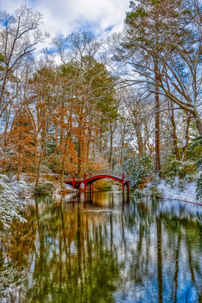 Red bridge over calm lake with snow dusted trees autumn winter colors serene landscape wallpaper