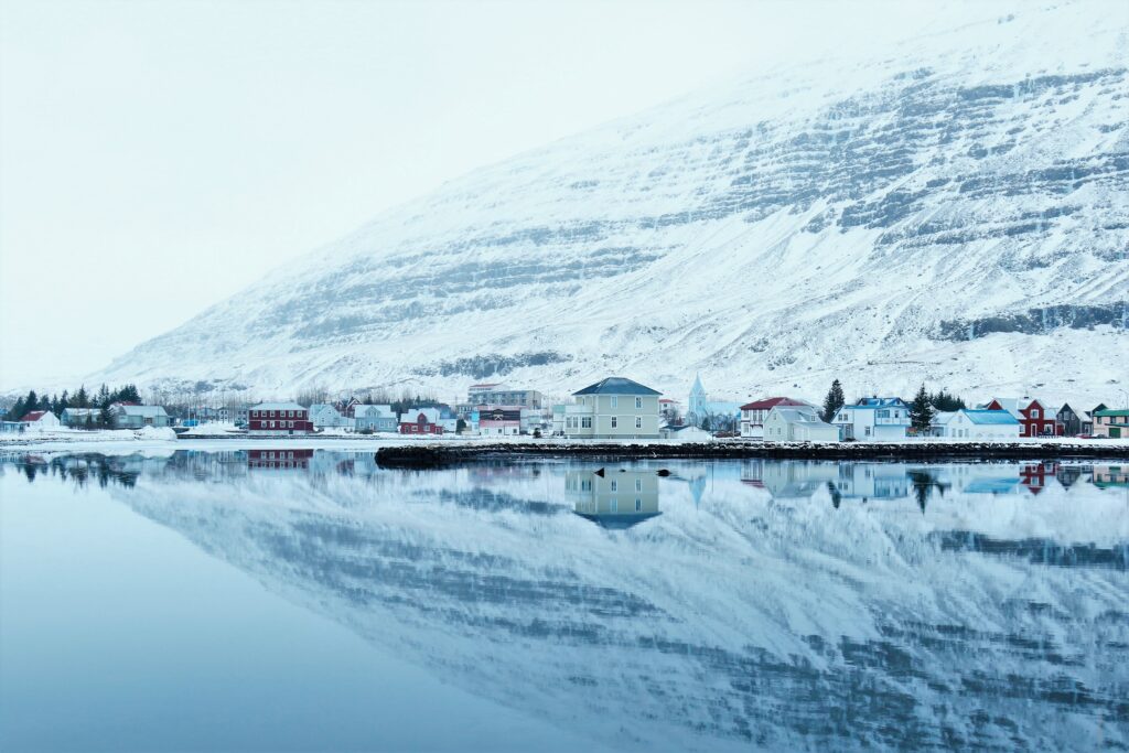 Serene winter wallpaper with quaint buildings by calm river and snow-covered hills reflection