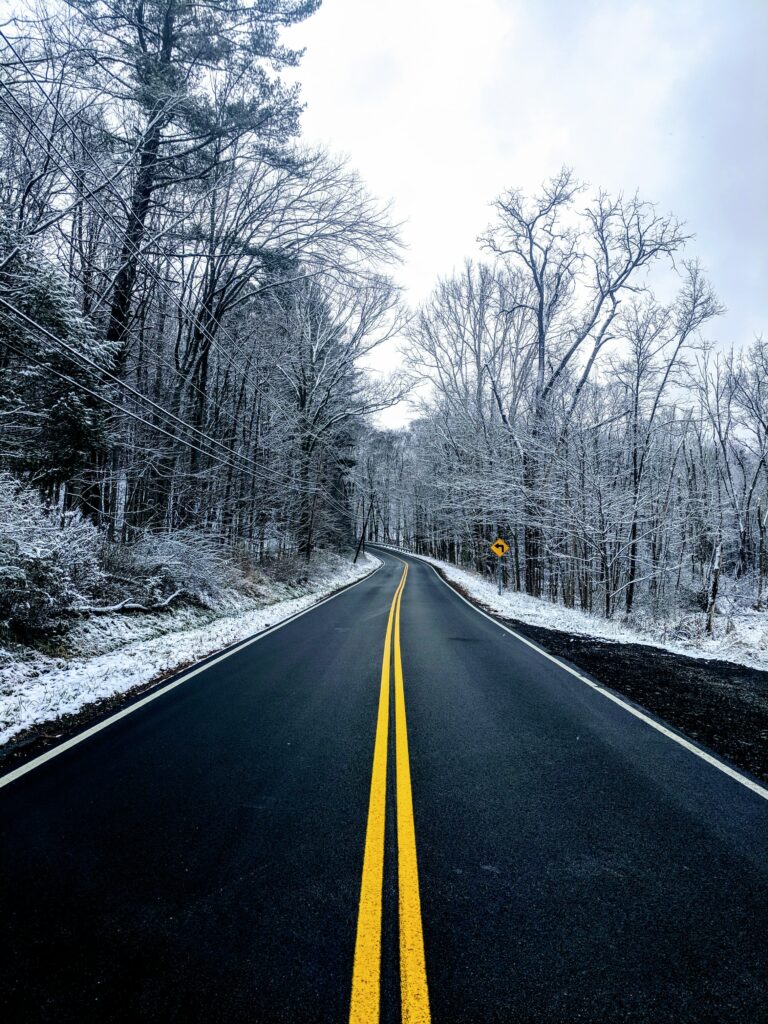 Winter wallpaper of empty asphalt road with yellow markings and snow covered trees under clouds