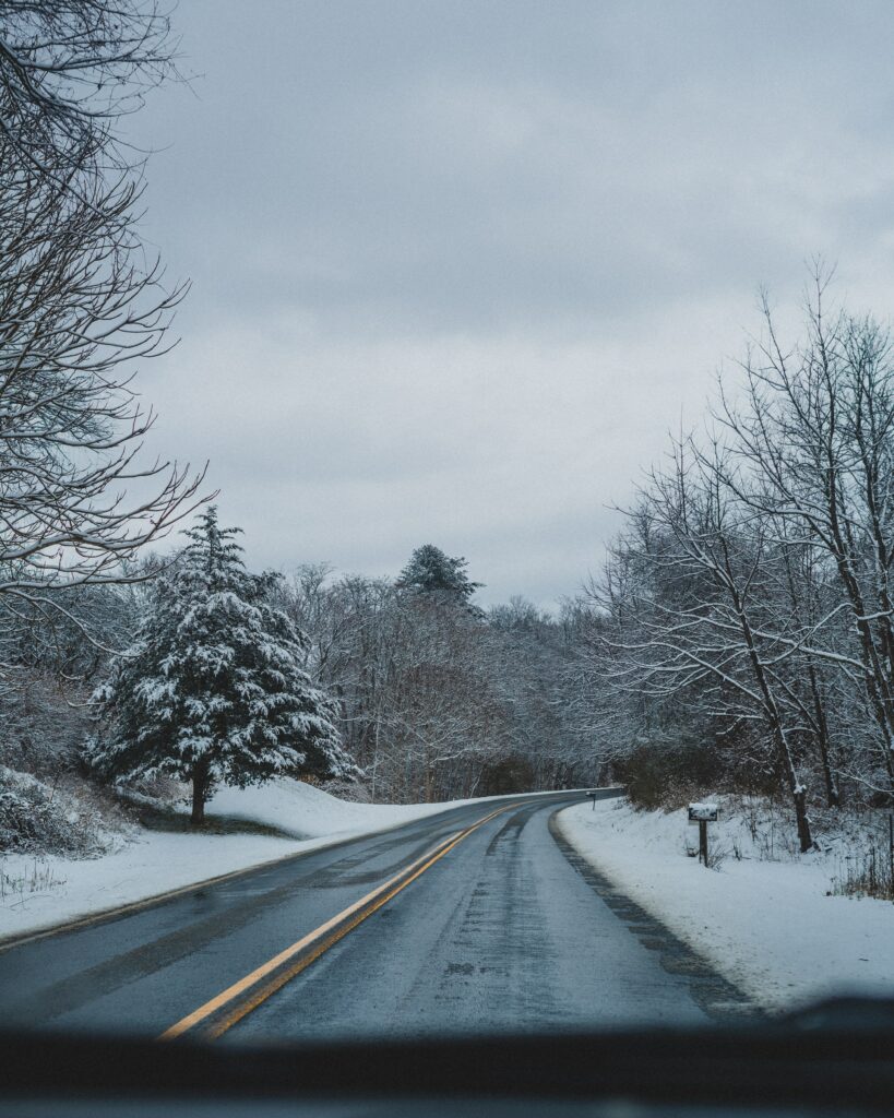 Winding asphalt road through snowy winter forest with snow dusted trees under cloudy sky wallpaper