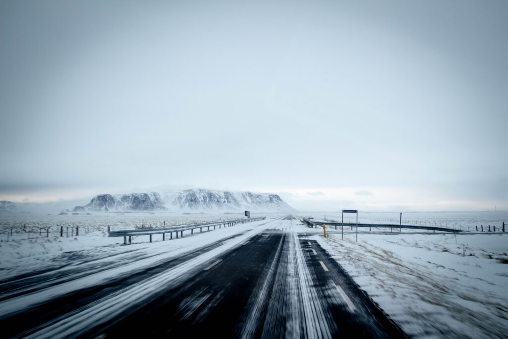 Snowy winter road stretching through icy fields toward distant mountains under soft light Wallpaper