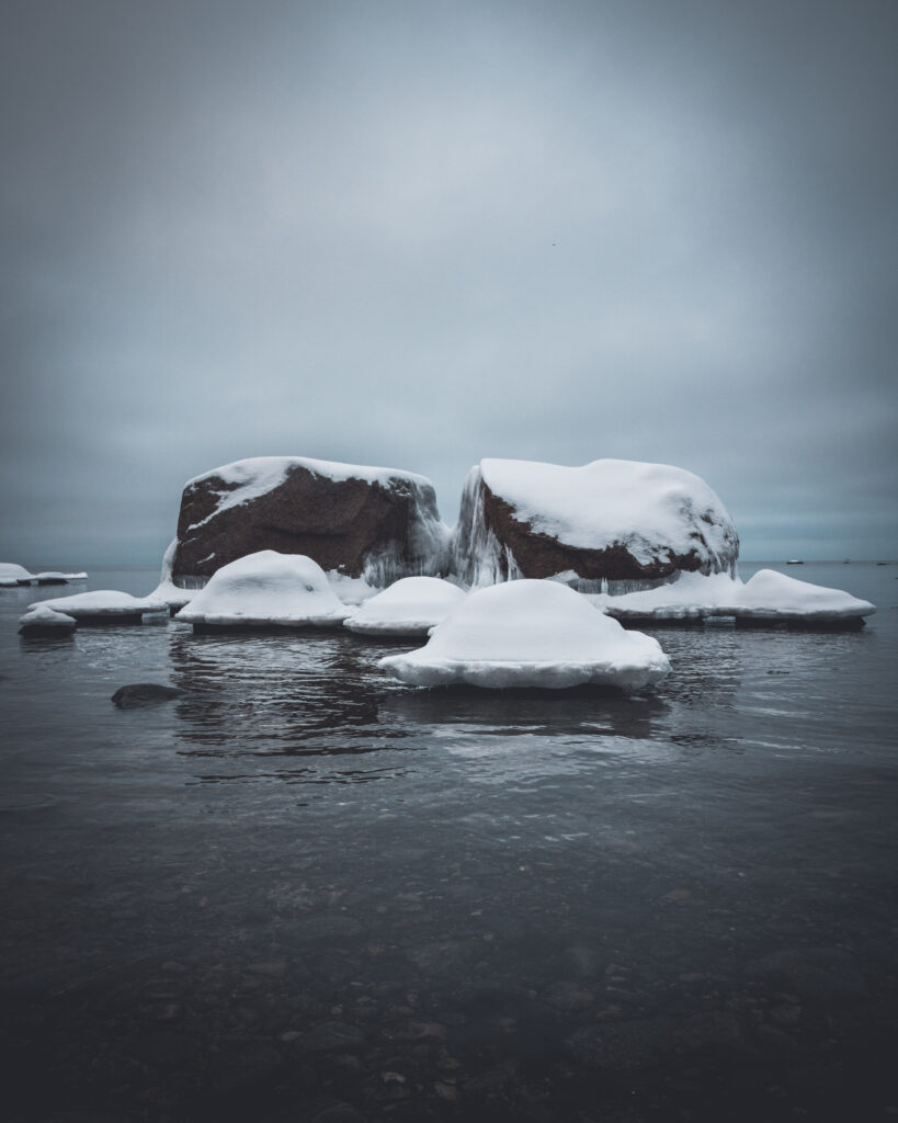 Snow covered stones and icy rocks in a calm winter sea under an overcast sky wallpaper background