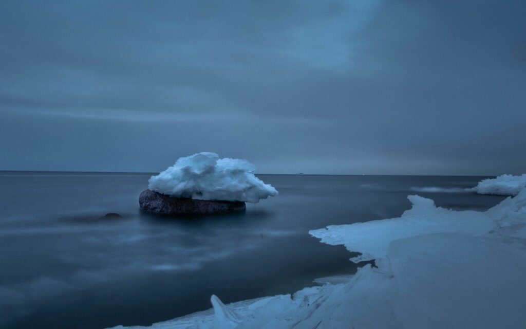 Serene winter seascape with snow covered stone calm misty waters cloudy blue gray sky wallpaper background