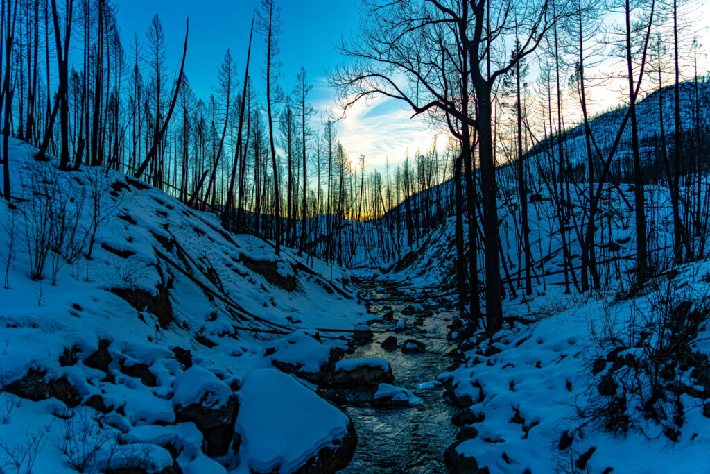 Serene winter landscape with snowy hills gentle stream and bare trees at sunset in cool blue tones Wallpaper