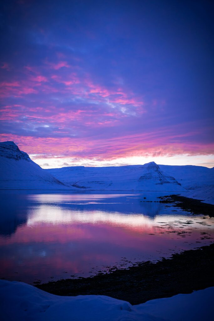 Winter sunset over snowy mountains and calm lake reflecting vibrant pink and purple hues Wallpaper