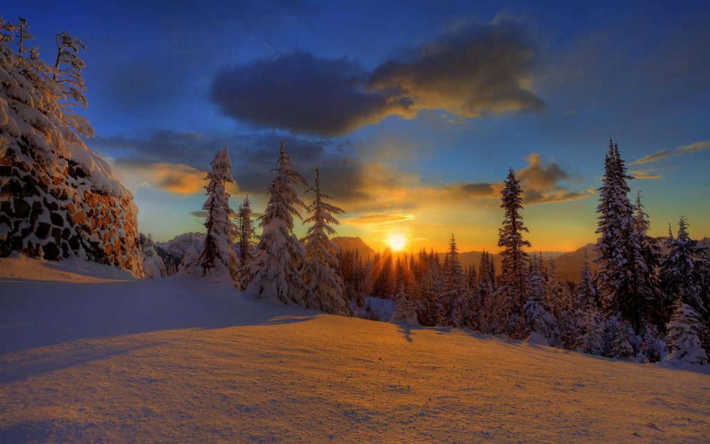 Snowy forest sunset with golden rays on pine trees and mountains serene winter desktop wallpaper