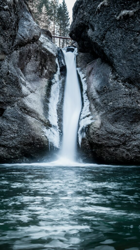 Serene waterfall flowing between icy rock cliffs with cool blue and gray winter tones wallpaper